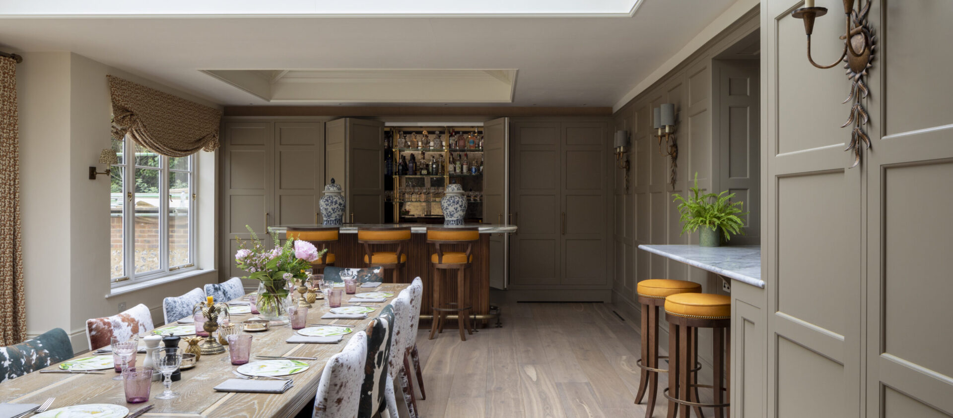 A bespoke cocktail bar sits at one end of an Orangery extension with large dining table and chairs