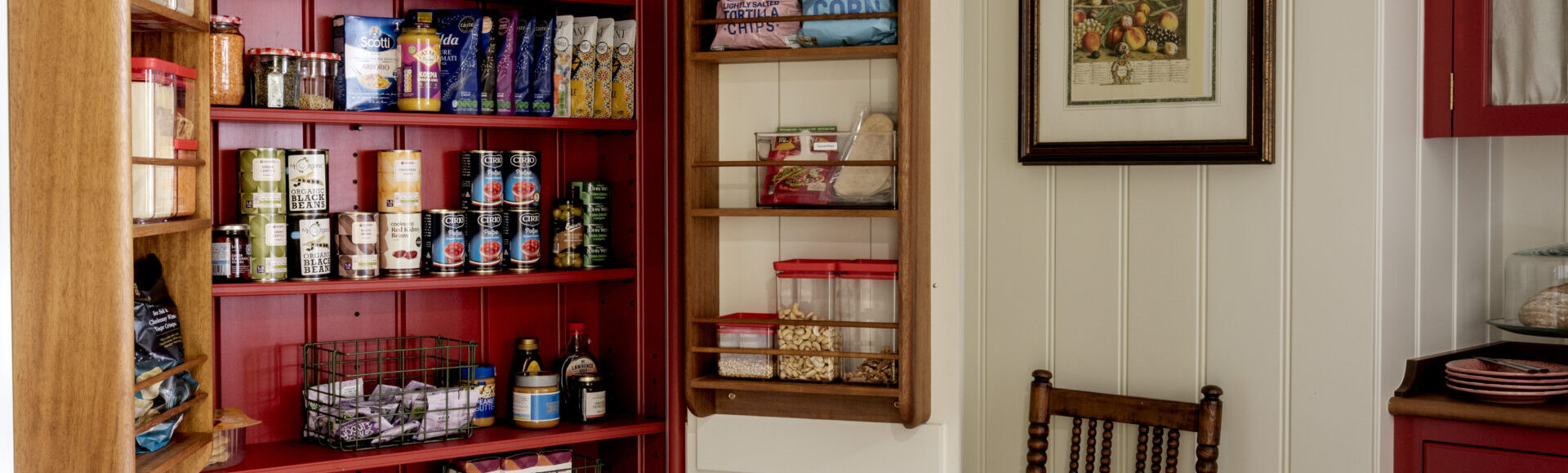 A kitchen pantry cupboard recessed in to a panelled wall with red hand painted interior