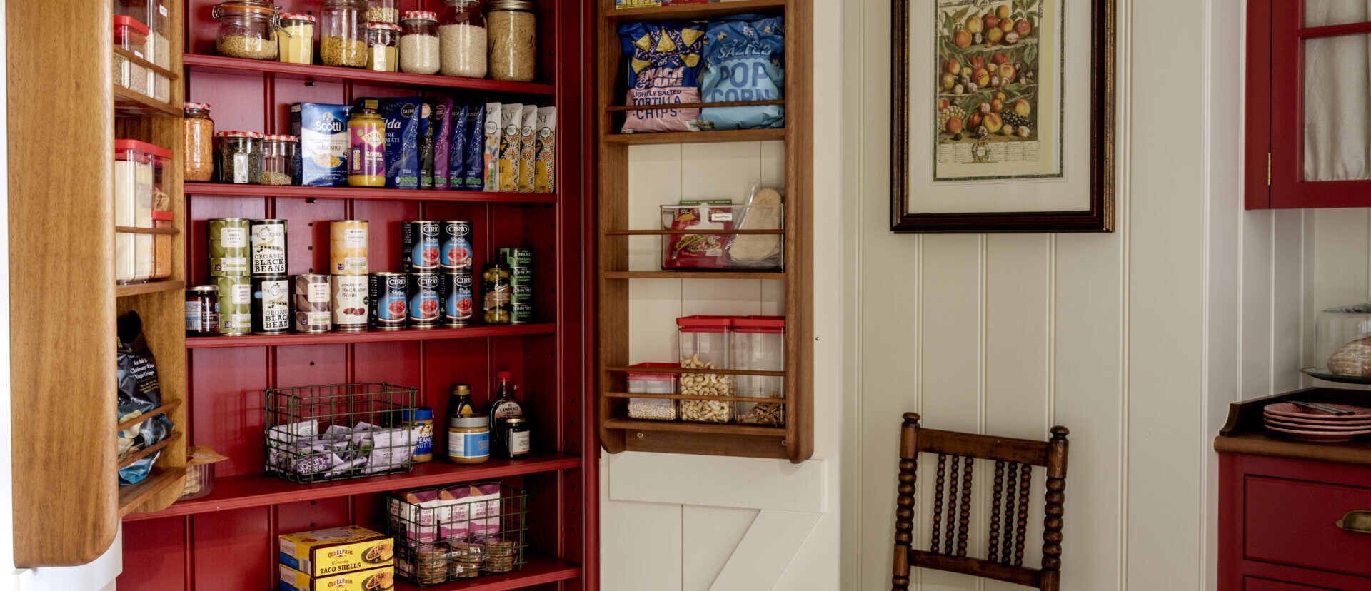 A kitchen pantry cupboard recessed in to a panelled wall with red hand painted interior