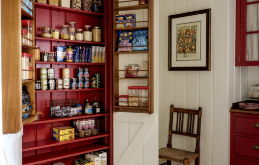 A kitchen pantry cupboard recessed in to a panelled wall with red hand painted interior