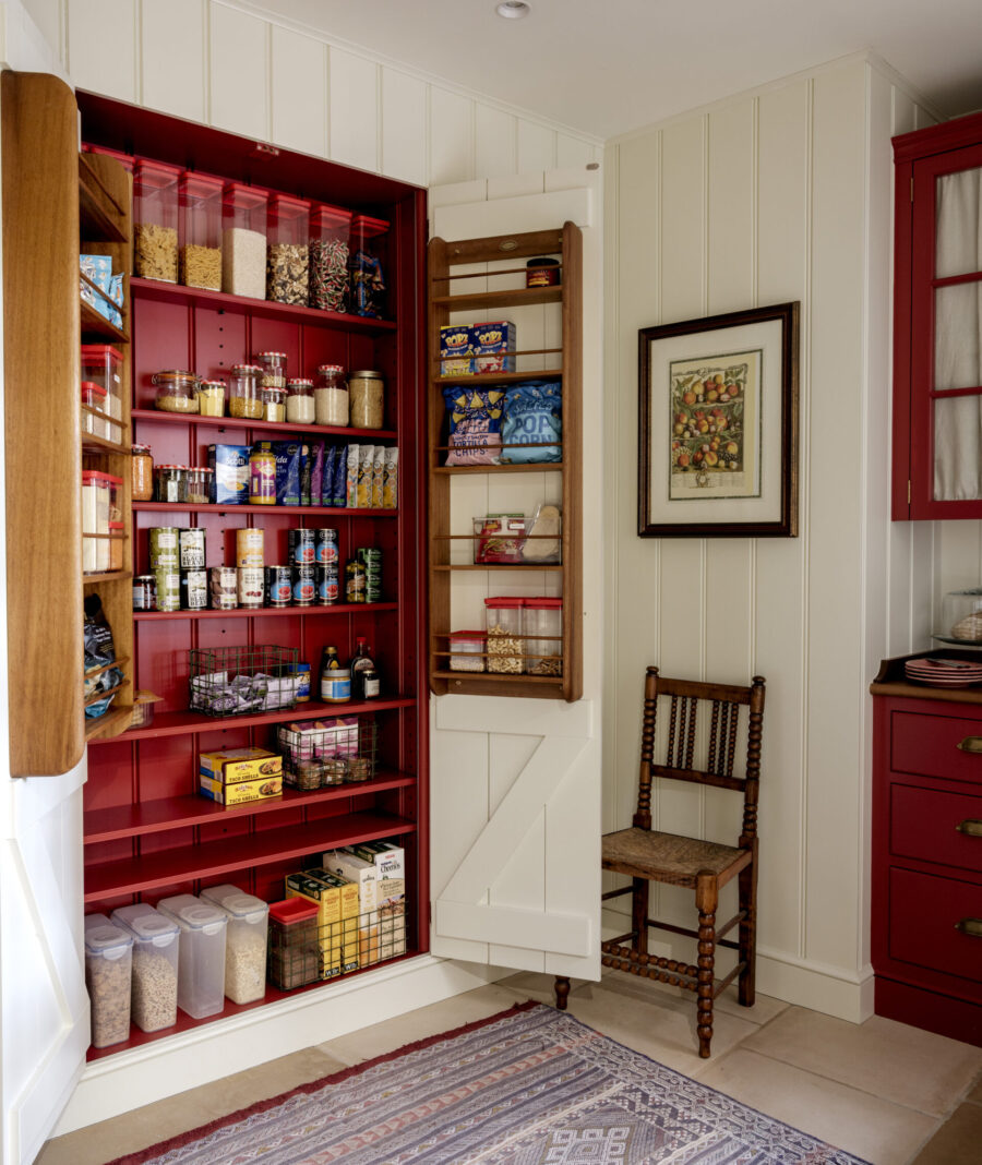 A pantry cupboard recessed in to a panelled wall with red hand painted interior