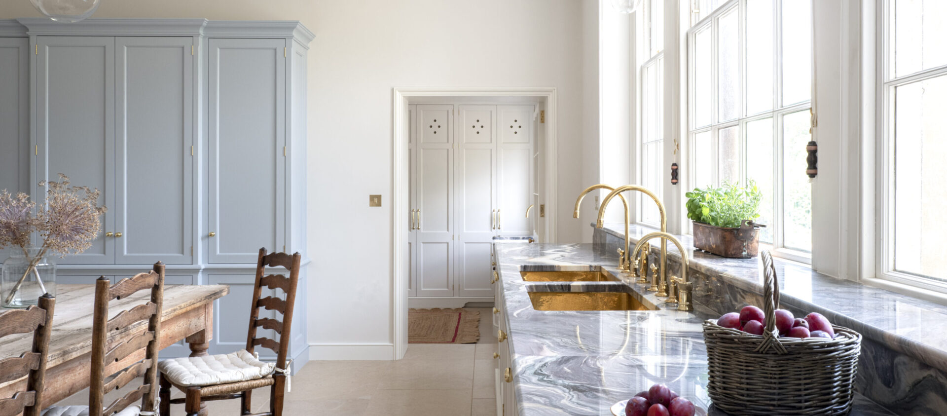 A pale blue cabinet at end of a Kitchen for a Regency Villa with a full length window with pale cabinetry underneath