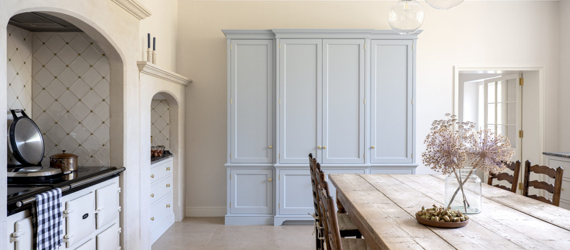 A bespoke Dorset kitchen design featuring blue bespoke kitchen house keeper's cabinet and an Aga set withiin a stone arch.