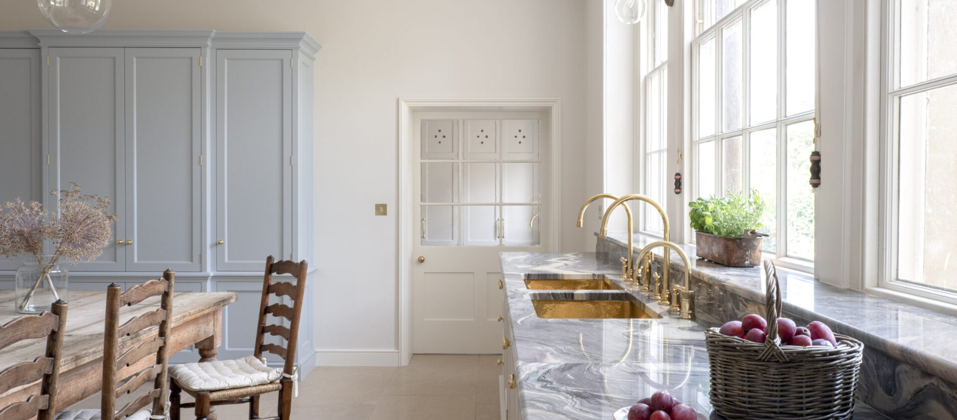 A pale blue cabinet at end of a Kitchen for a Regency Villa with a full length window with pale cabinetry underneath