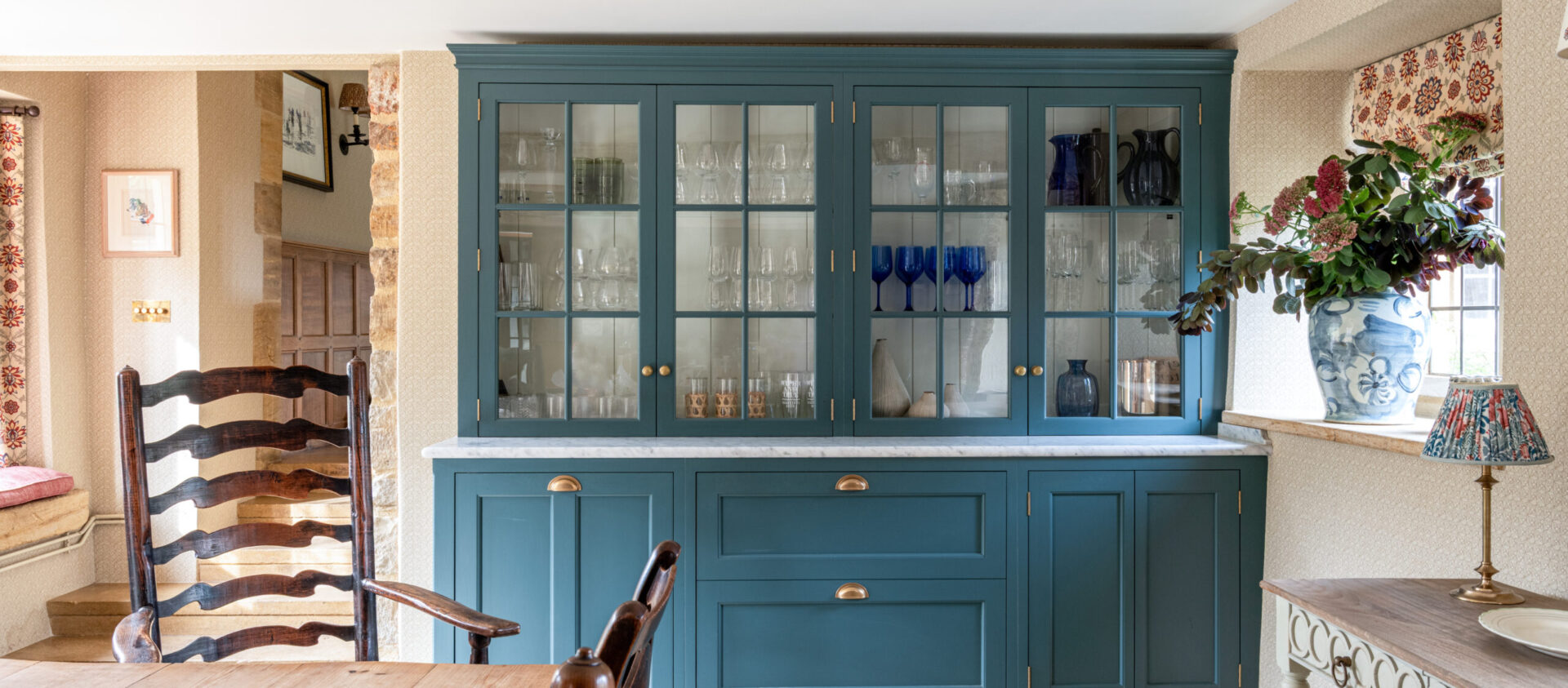 A blue hand painted bespoke kitchen dresser with glazed cabinets above drawers in Devon