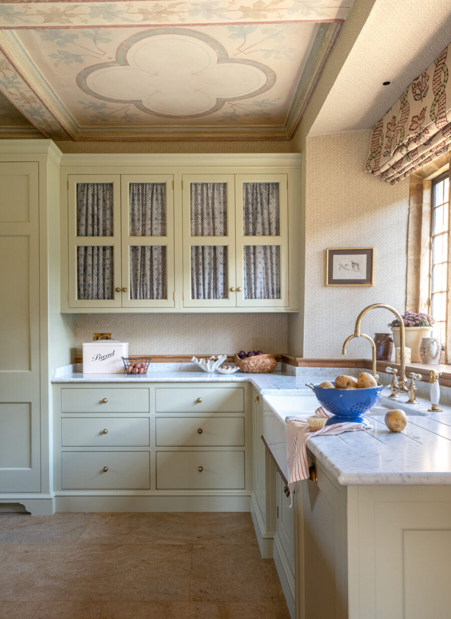 Cream coloured glazed wall cabinets in a handmade kitchen with curtains behind glass. Cream coloured glazed wall cabinets in a handmade kitchen with curtains behind glass.